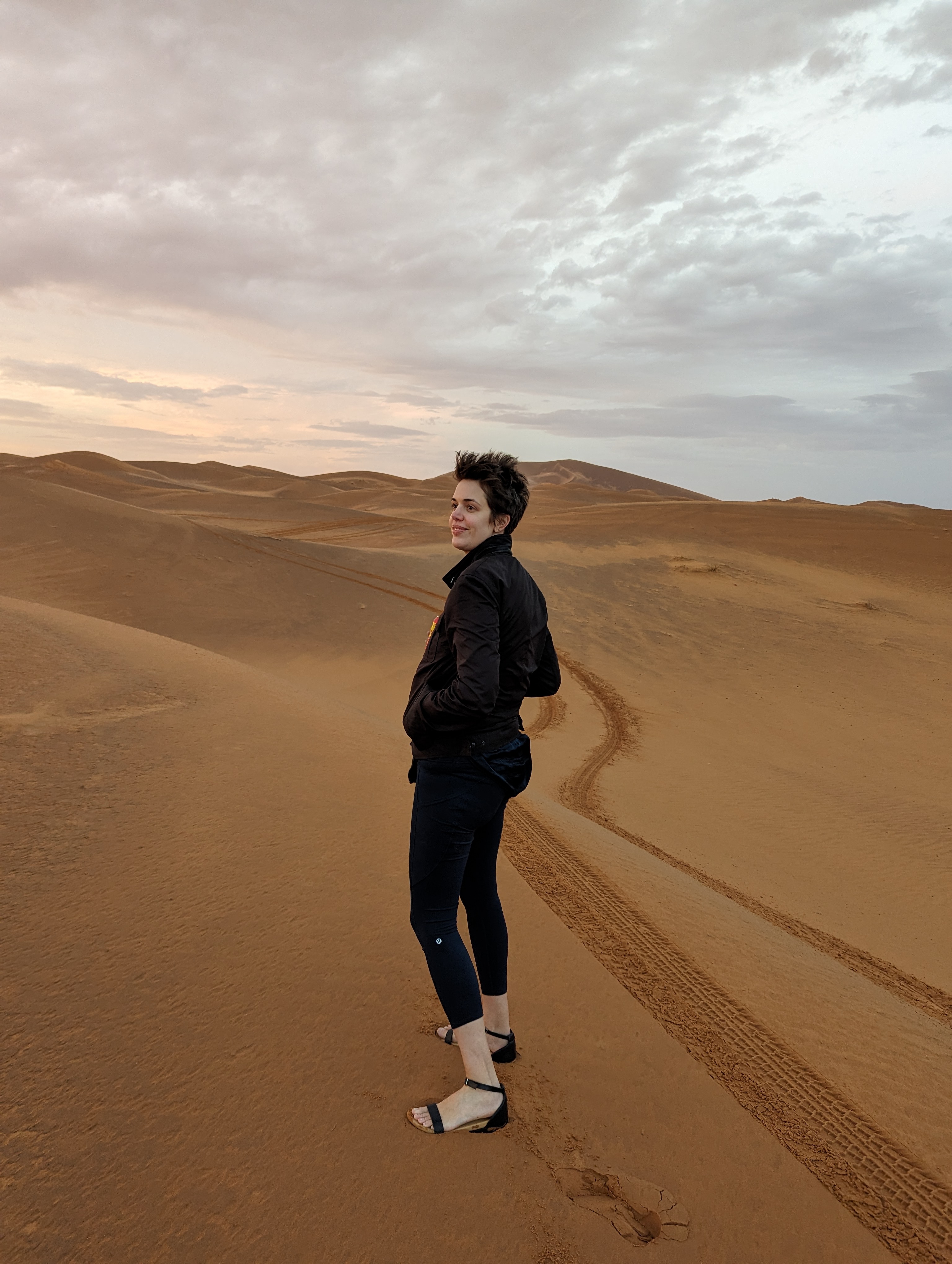 Brooks Bell standing on the Sahara desert dunes, looking back over her shoulder